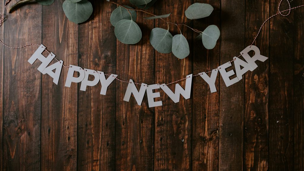A "Happy New Year" banner hangs on a wooden wall with eucalyptus branches above it.