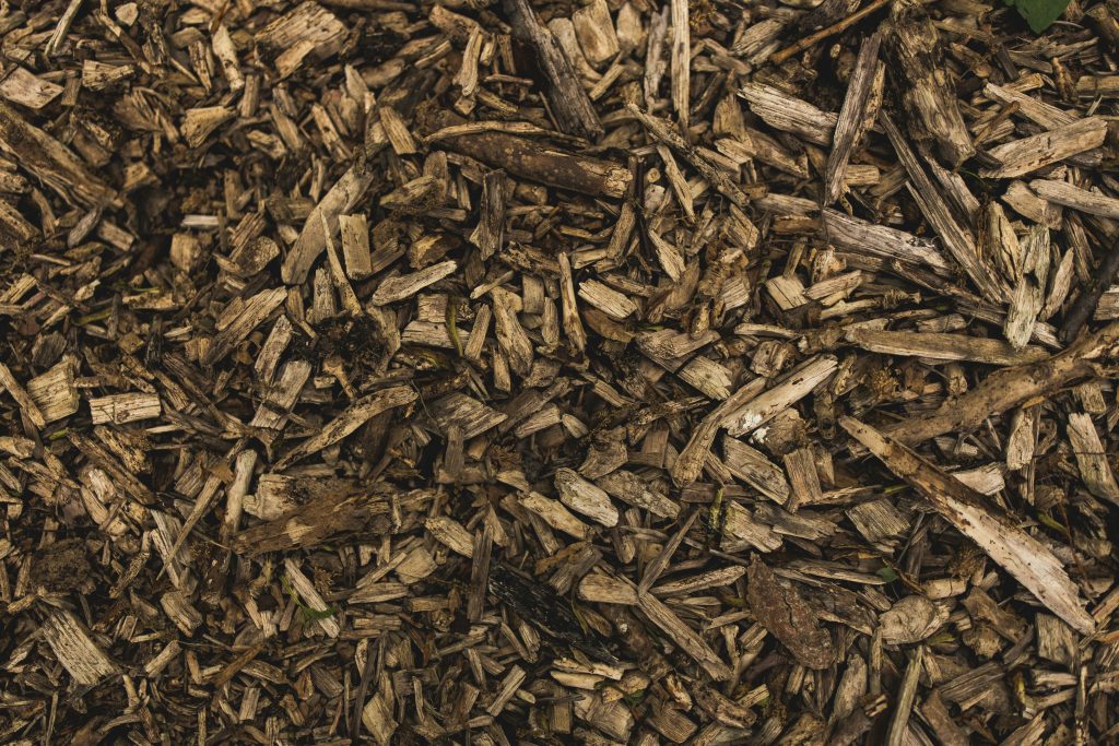 A close-up view of a pile of brown wood chips and mulch, showing rough, textured pieces of various sizes.