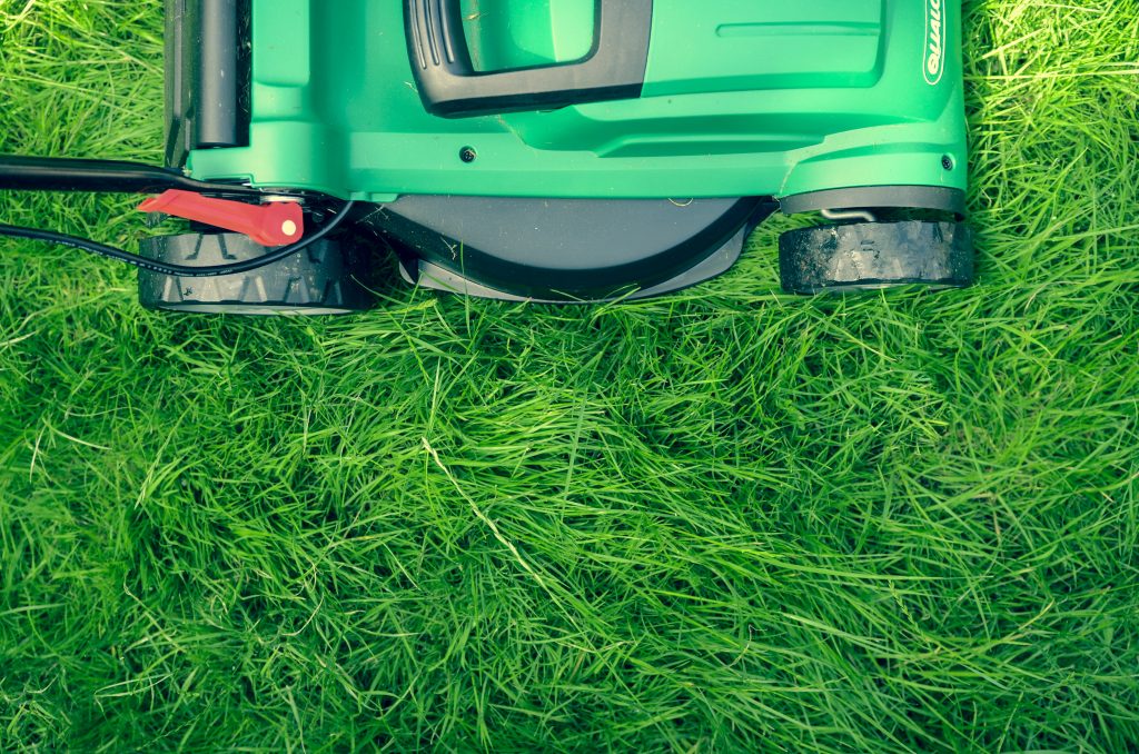 Close-up of a green lawn mower cutting grass, with freshly cut and uncut grass visible beneath and around the mower.
