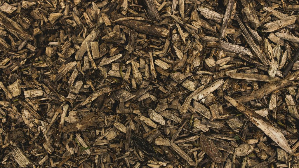 A close-up view of a pile of wood chips and bark mulch, showing various sizes and textures of natural brown wood pieces.